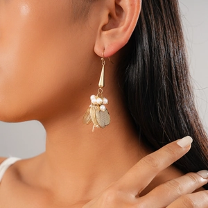 Detailed view of long gold drop earrings with white pearls on a model wearing them