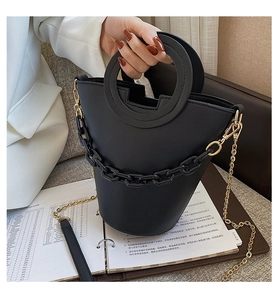 Detail of a black bucket bag featuring a unique circular cutout handle and chunky chain