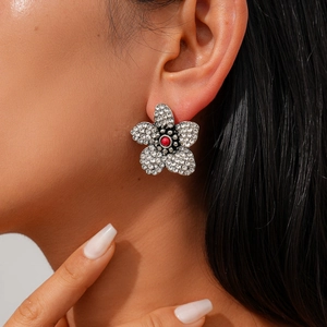Nahaufnahme glitzernder Blumenohrstecker mit Silberblüten und roter Mittelperle