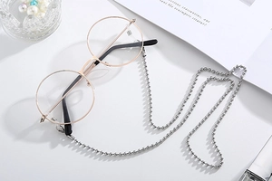 Close-up of a silver beaded chain on gold round frame glasses with luxury props