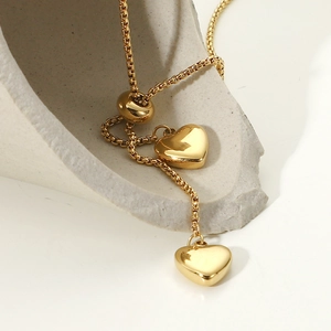 Collana a Y dorata con doppio ciondolo a cuore presentata su una base di pietra