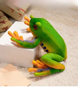 Detailed view of plush green tree frog doll with red eyes and orange limbs on gift box