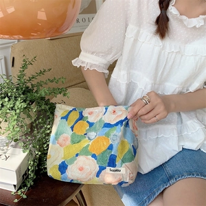 Detailed close-up of a floral cotton makeup bag held by a person in a cozy indoor setting