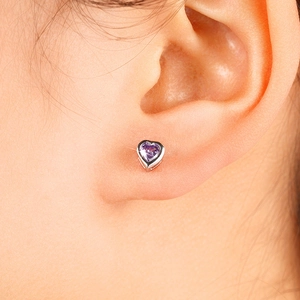 Macro shot of a silver claw-set heart earring with a faceted purple crystal on earlobe