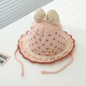 Detail der rosa Babystrickmütze mit Spitzenborte, Jacquardmuster und Kirsch-Anhängern