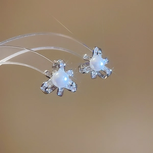 Detail view of pearl earrings with crystal bow design on a warm brown background
