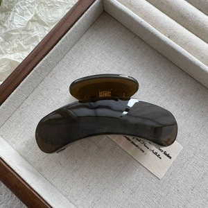 Detailed view of a dark brown glossy hair claw clip on a wooden jewelry display tray