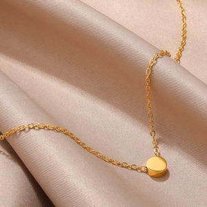Detailed close-up of a minimalist gold pendant necklace on champagne silk fabric