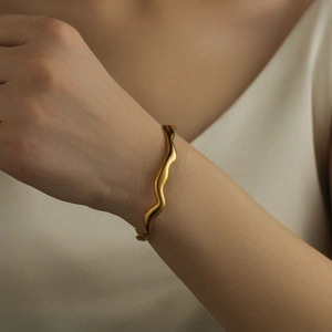 Close-up of elegant gold wave pattern bangle with matte finish on a model's wrist