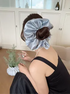 Macro detail of oversized silver-grey satin scrunchie on a low ponytail hair tie