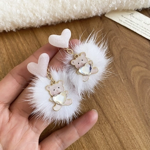 Detail of white fluffy pom-pom earrings with a cute pink heart stud and bear pendant