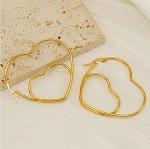 Detail of gold double heart hollow earrings on beige stone and textured background