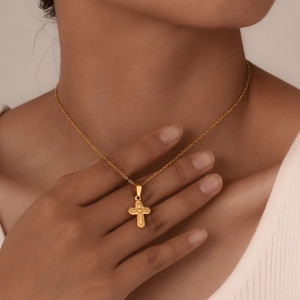 Close-up of a gold cross necklace with embossed texture worn by a model in soft light