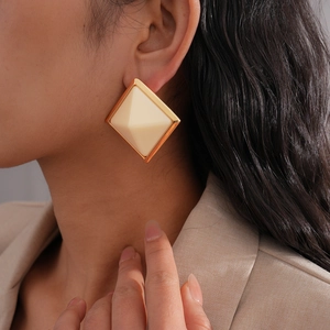 Detail of square geometric resin stud earring with gold metallic edge on a model's ear