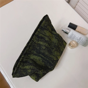 Green and black jacquard toiletry bag with skincare products on a white surface