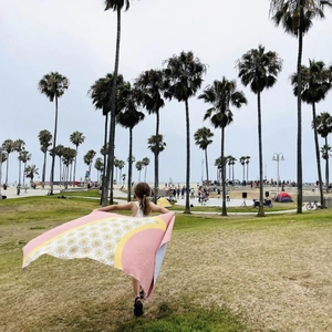 Girl unfolding a floral daisy beach towel in a tropical park with palm trees