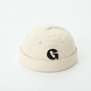 Detail of beige canvas docker hat with black 3D embroidered letter G on white background