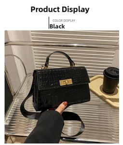 Detail of black crocodile texture handbag with gold twist lock and wide canvas strap