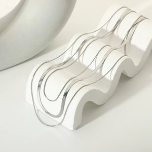 Detailed view of sleek silver flat snake chain necklace on white wave pedestal