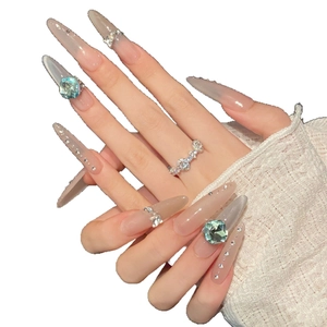 Long pointed press-on nails with nude pink cat-eye effect and blue gemstones