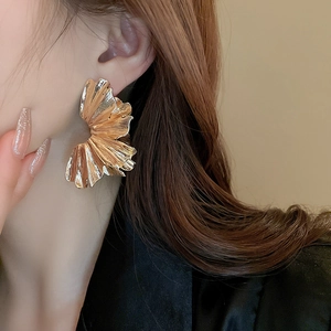 Detailed view of large gold pleated flower petal earrings with textured metal finish