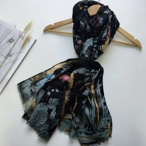 Detail of floral satin scarf with gold accents and elegant fringe on a wooden hanger