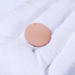 Polished rose gold stainless steel round charm pendant on a white gloved palm