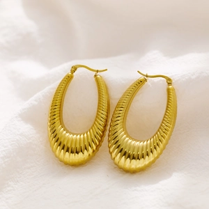 Detailed view of gold oval ribbed earrings with a textured surface on white fabric