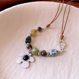 Detail of beaded necklace with silver flower pendant and natural stone beads on a ceramic tray