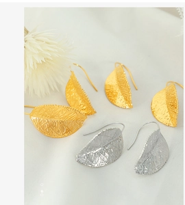 Detailed macro view of gold and silver leaf earrings with hollowed metal texture