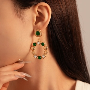 Close-up of vintage gold earrings with green gems and crystals on a female model