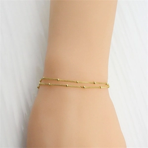 Detail of minimalist gold double-layered beaded chain bracelet on model's wrist