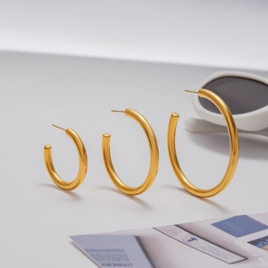 Three gold stainless steel hoop earrings in small medium and large sizes on a clean desk