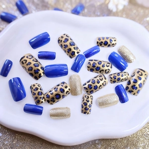 Blue leopard print and gold glitter press-on nails set on white ceramic tray