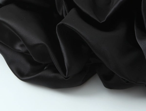 Close-up of high-gloss black satin fabric with elegant lace stitching and smooth texture