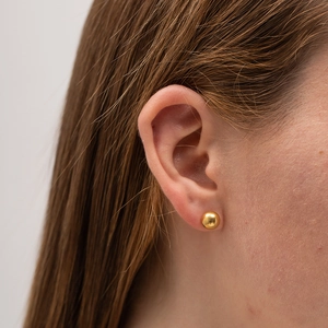 Minimalist golden metal ball stud earrings worn by a female model in a side-view close-up