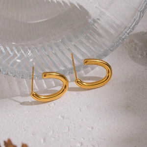 Detail view of gold U-shaped earrings on textured surface with glass shadow effects
