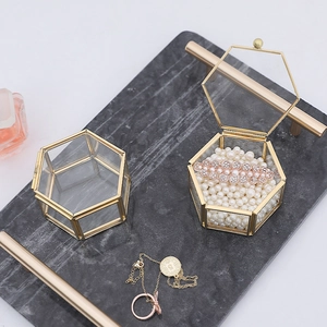 Luxury hexagonal glass jewelry box with gold metal frame on a marble tray