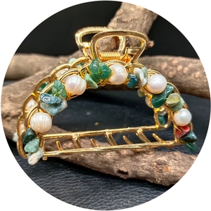Golden hair claw with green natural stones and pearls shown on a dark rustic background