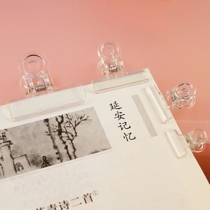 Macro shot of four transparent heart-shaped plastic clips holding paper on a pink background