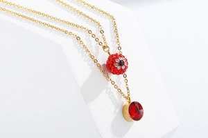 Detail of gold double-layer necklace featuring a red rhinestone sphere and crystal pendant