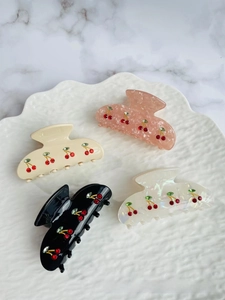 Detailed view of four acetate hair claws with sparkling red rhinestone cherry patterns
