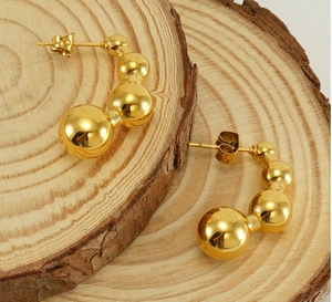 Dettaglio degli orecchini a lobo a forma di C dorati su un supporto in legno naturale