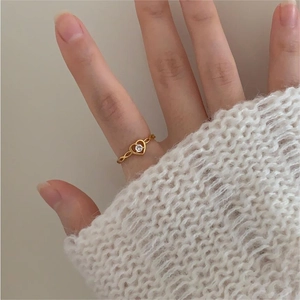 Close-up of a golden heart-shaped zircon ring worn on a finger with white sweater