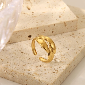 Détail macro d'une bague ouverte ondulée plaquée or sur pierre de travertin beige texturée