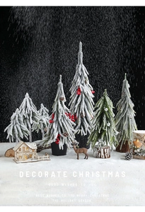 Close-up of artificial snow-flocked Christmas trees with red berries and a cozy wooden cabin