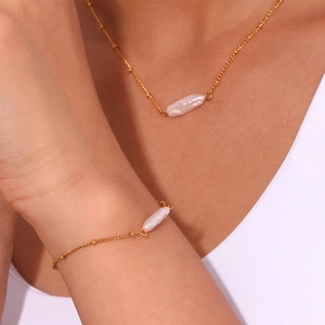 Detailed view of model wearing a gold beaded chain set with baroque pearl pendants
