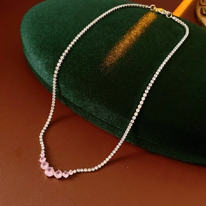 Detail of silver necklace with five gradient pink gemstones on green velvet background