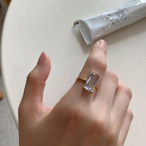 Detailed view of gold band ring featuring a rectangular zircon stone on a female hand
