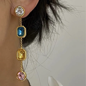 Boucles d'oreilles pendantes avec pierres carrées colorées et chaînes dorées sur modèle
